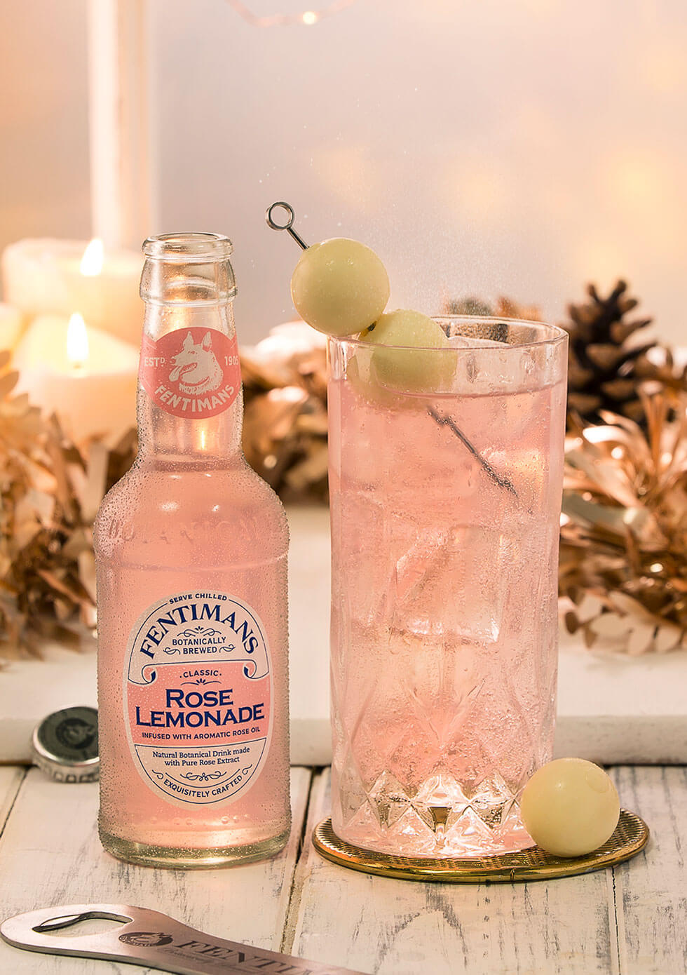 A bottle of Fentimans Rose Lemonade with a highball cocktail garnished with white chocolate balls